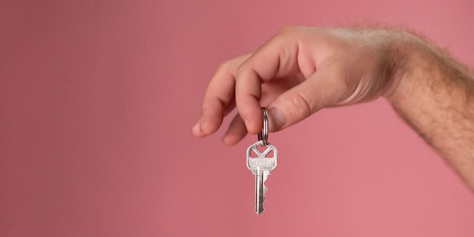 Hand holding a key over a pink background